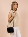 Audrey Mini, Black Leather cross body. Square shape with an adjustable leather strap. Model product image.