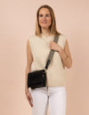 Audrey Mini, Black Leather cross body. Square shape with an adjustable checkered strap. Model product image.