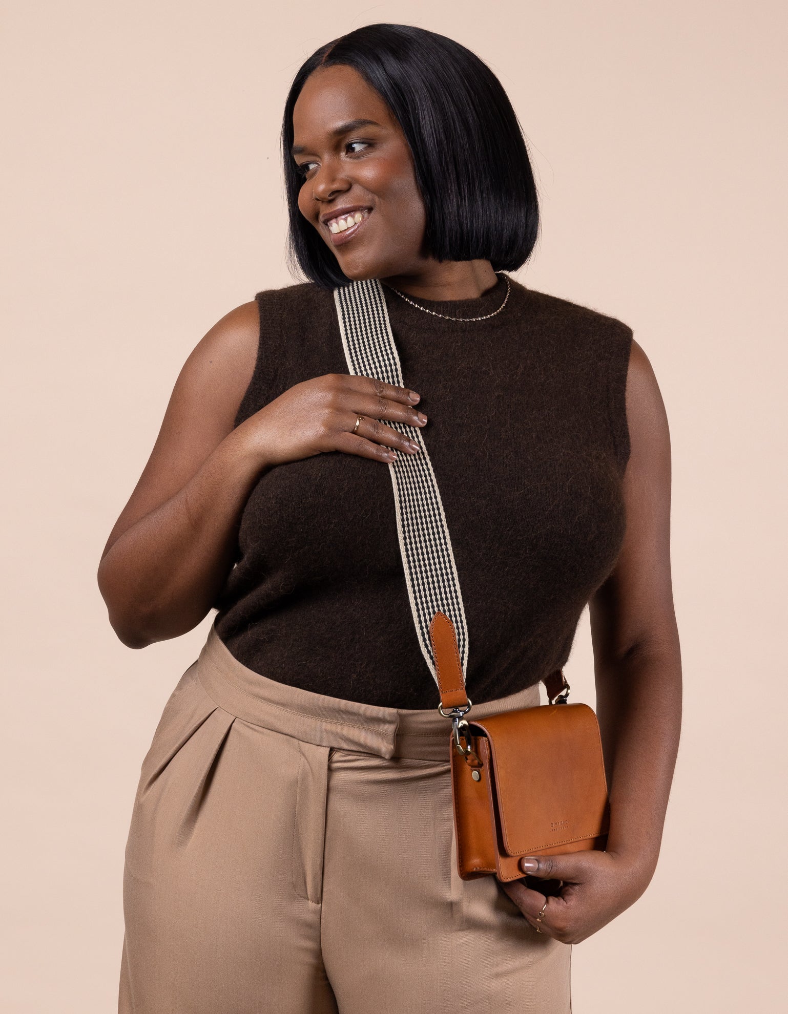 Audrey Mini Cognac leather bag. Square shape with an adjustable webbing strap. Model image