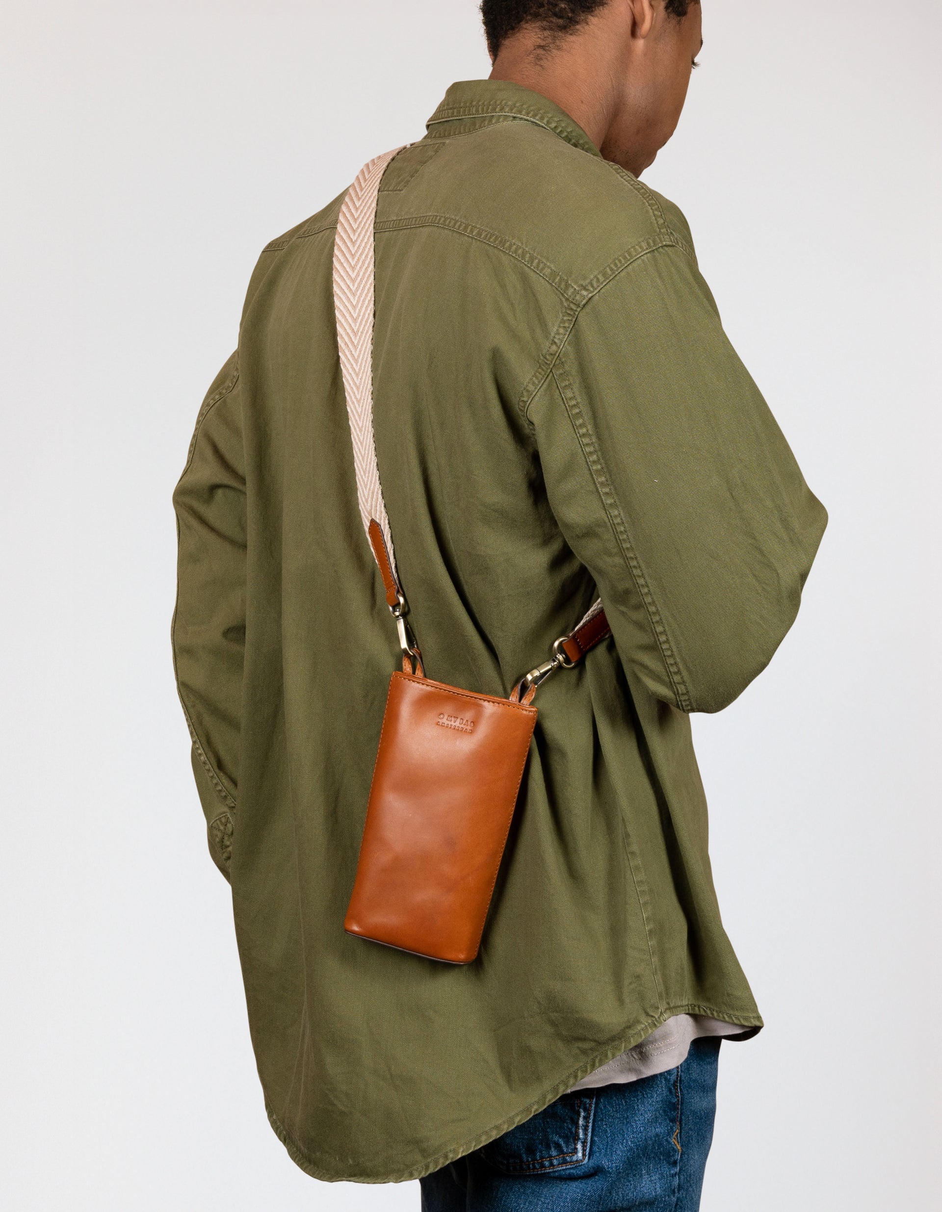 Charlie phone bag - cognac classic leather - male model back product image with organic cotton webbing strap