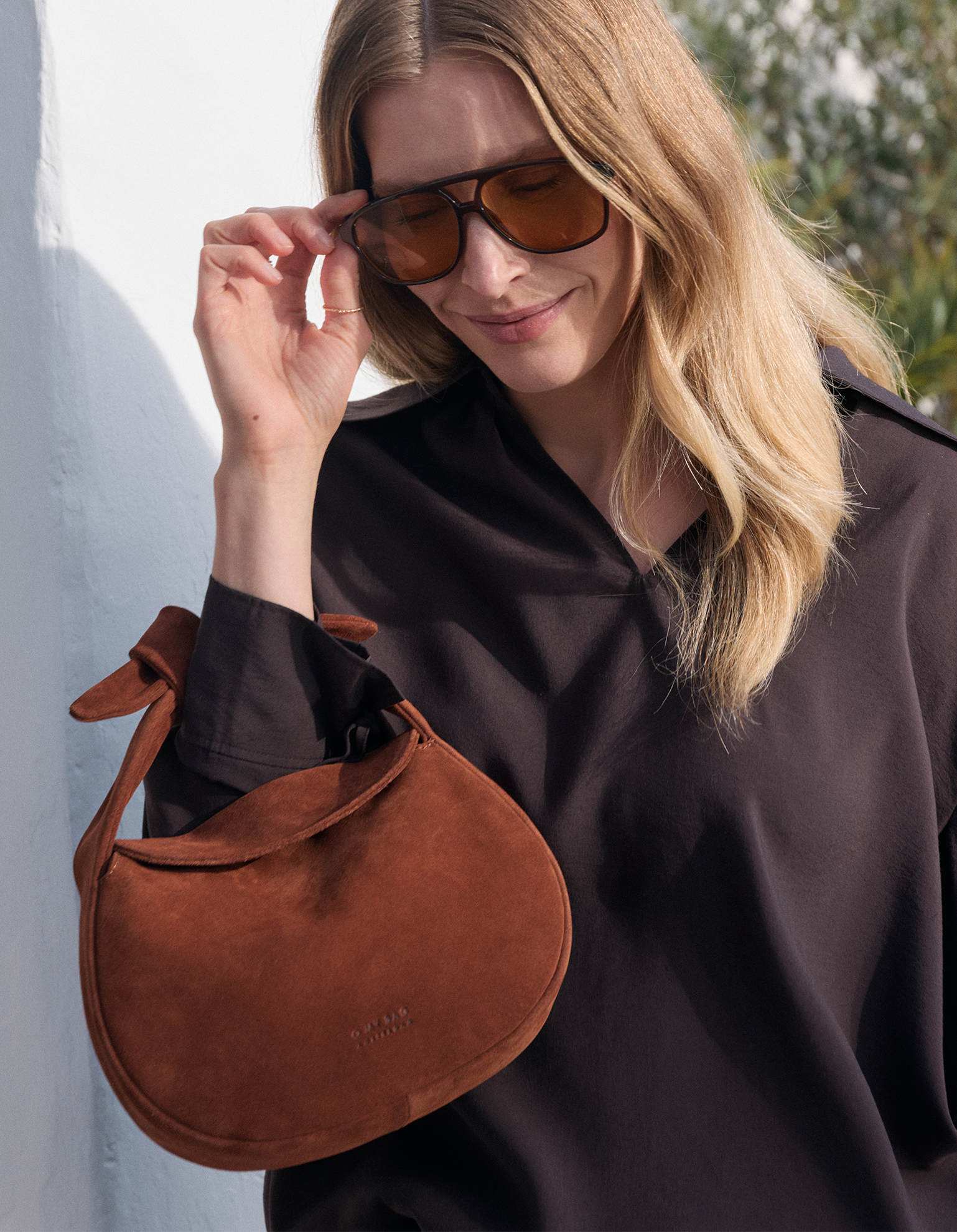 Model with brown bag and holding sunglasses