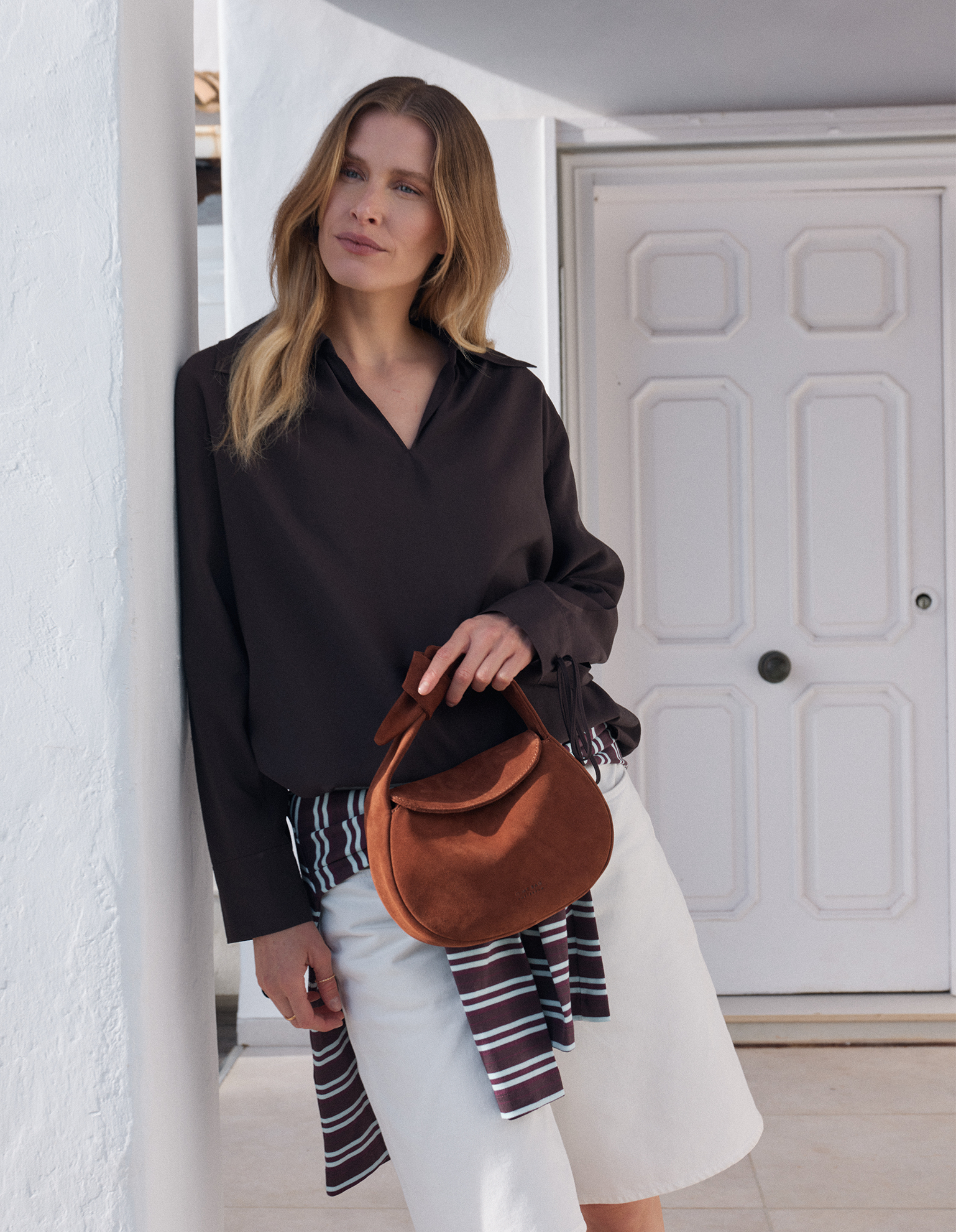 Model holding brown bag with summery outfit and door in background