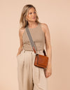 Model image of Audrey Mini cognac classic leather crossbody bag with adjustable checkered webbing strap