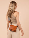 Model image of Audrey Mini cognac classic leather crossbody bag with adjustable checkered webbing strap