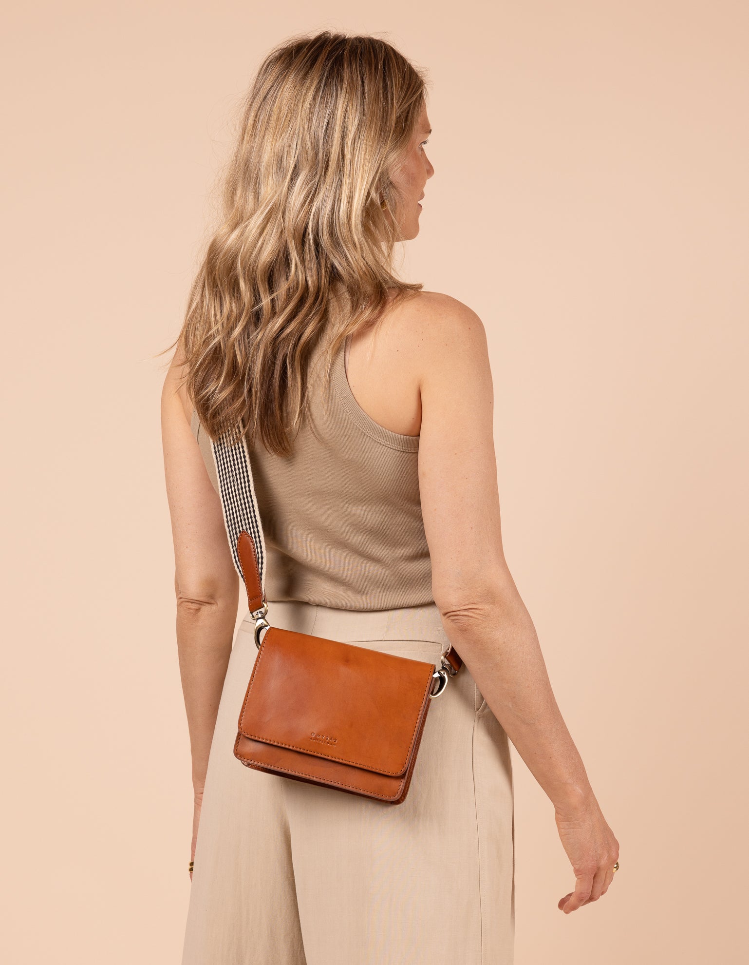 Model image of Audrey Mini cognac classic leather crossbody bag with adjustable checkered webbing strap