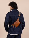 Becks Bum Bag in cognac with the adjustable checkered webbing strap. Male model product image.