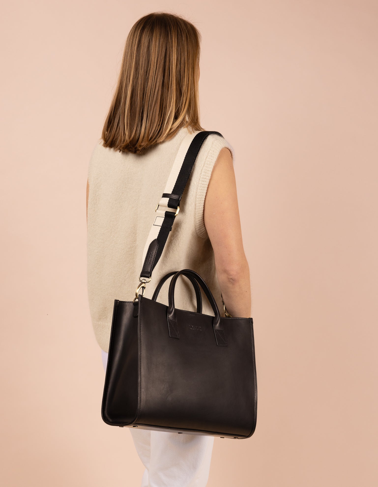 Rectangle shaped black leather tote bag with black and white strap - model image