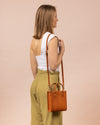 Small leather mini tote bag in brown with a thin long shoulder strap, model image