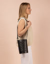 Image of model holding circular woven bucket bag in black leather. Side angle shot.
