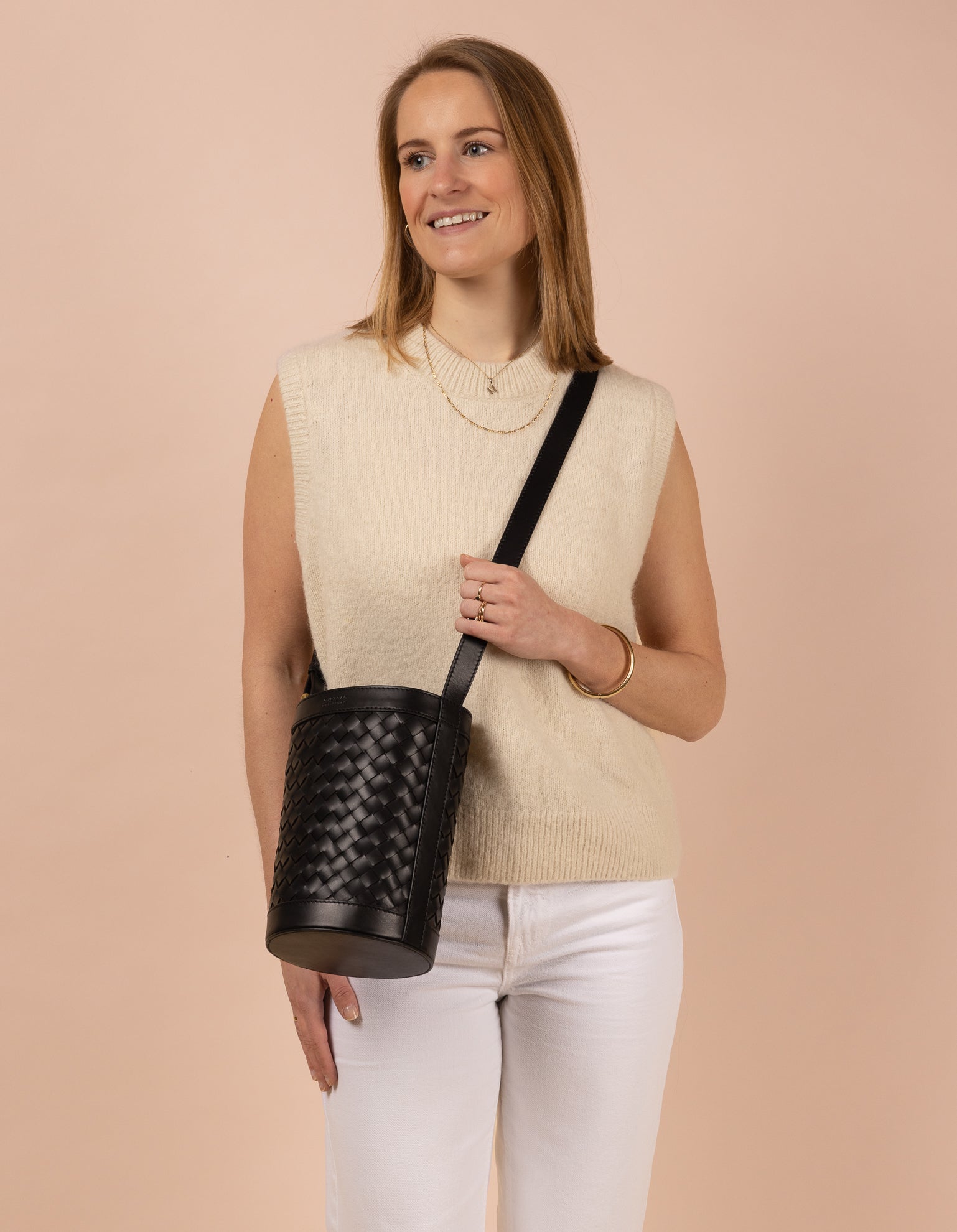 Image of model holding circular woven bucket bag in black leather. Front shot.