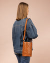 Image of model holding circular woven bucket bag in cognac leather. Worn on the shoulder.