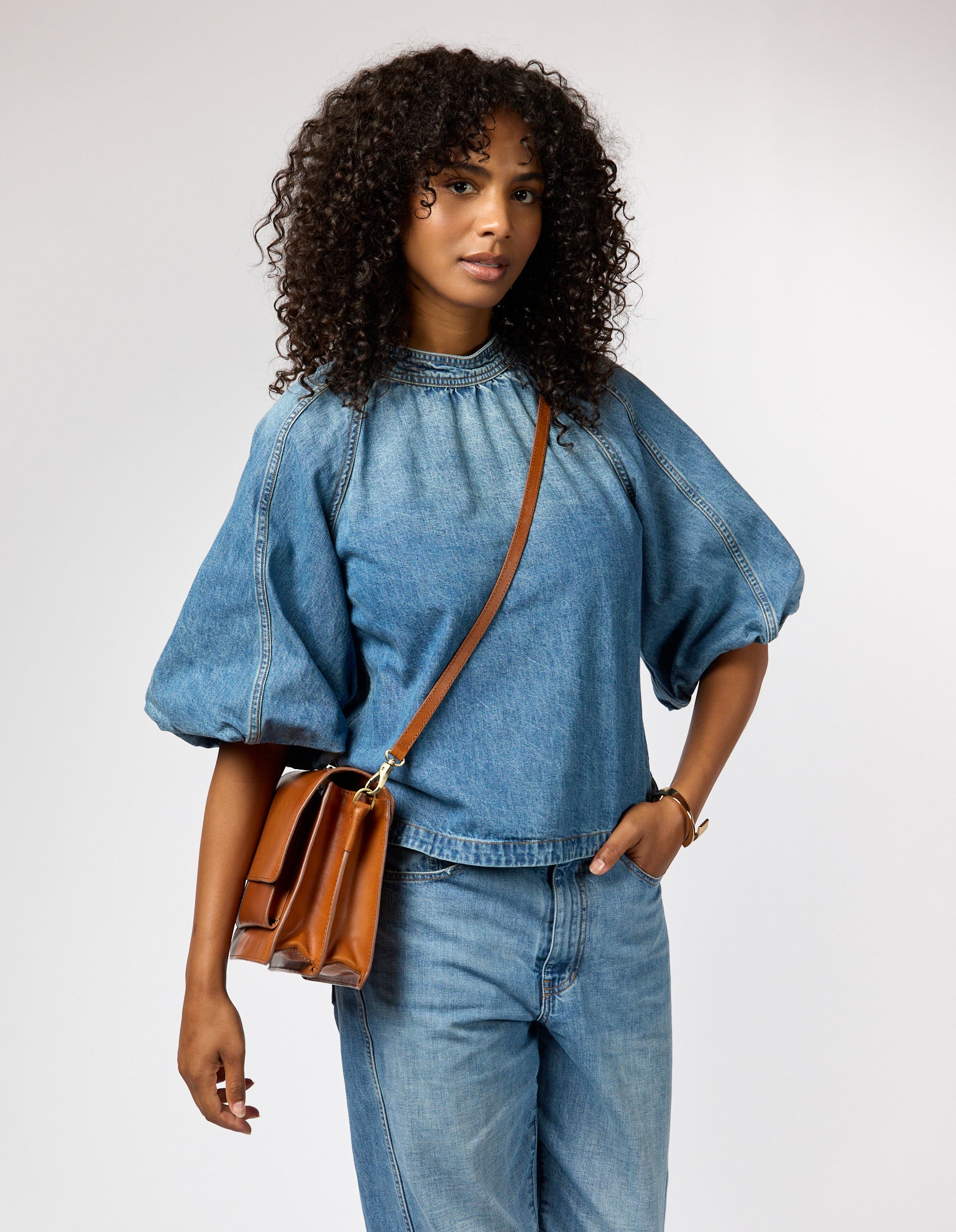 Female model wearing denim outfit with brown leather crossbody bag