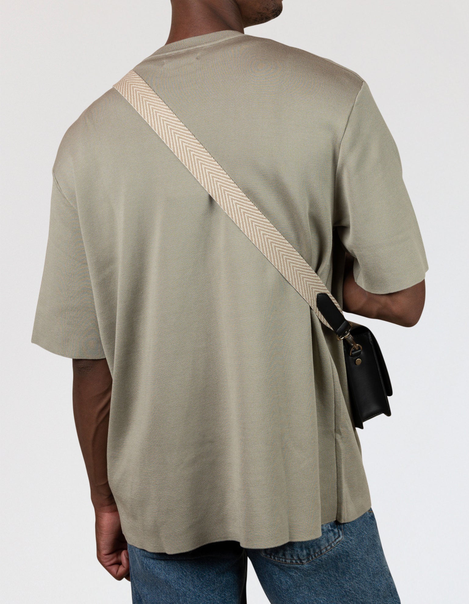 Herringbone Webbing Strap in Sand with black apple leather details. Male model product image, back view.