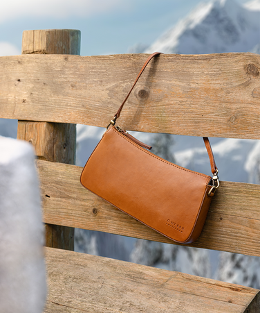 Brown leather bag on a wooden fence with snowy mountains in the background