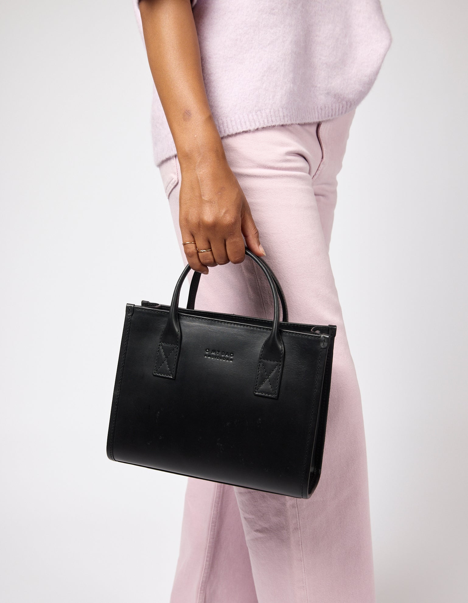 Person holding a black handbag against a white background