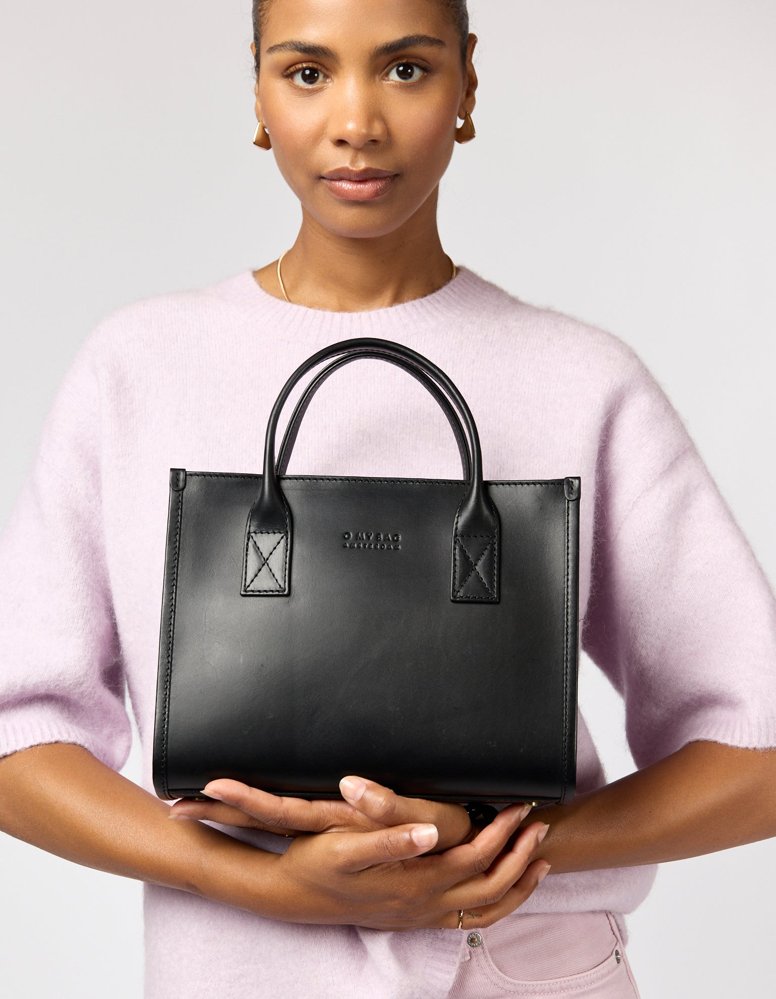 Woman holding a black handbag with a visible brand logo against a plain background