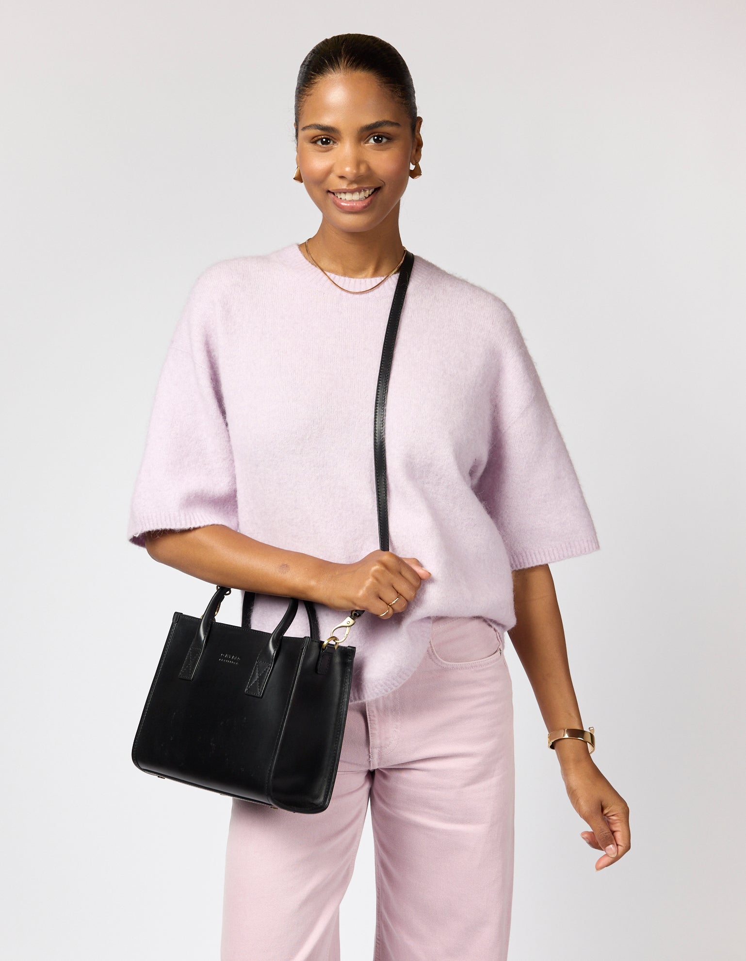 Woman holding a black handbag against a light gray background