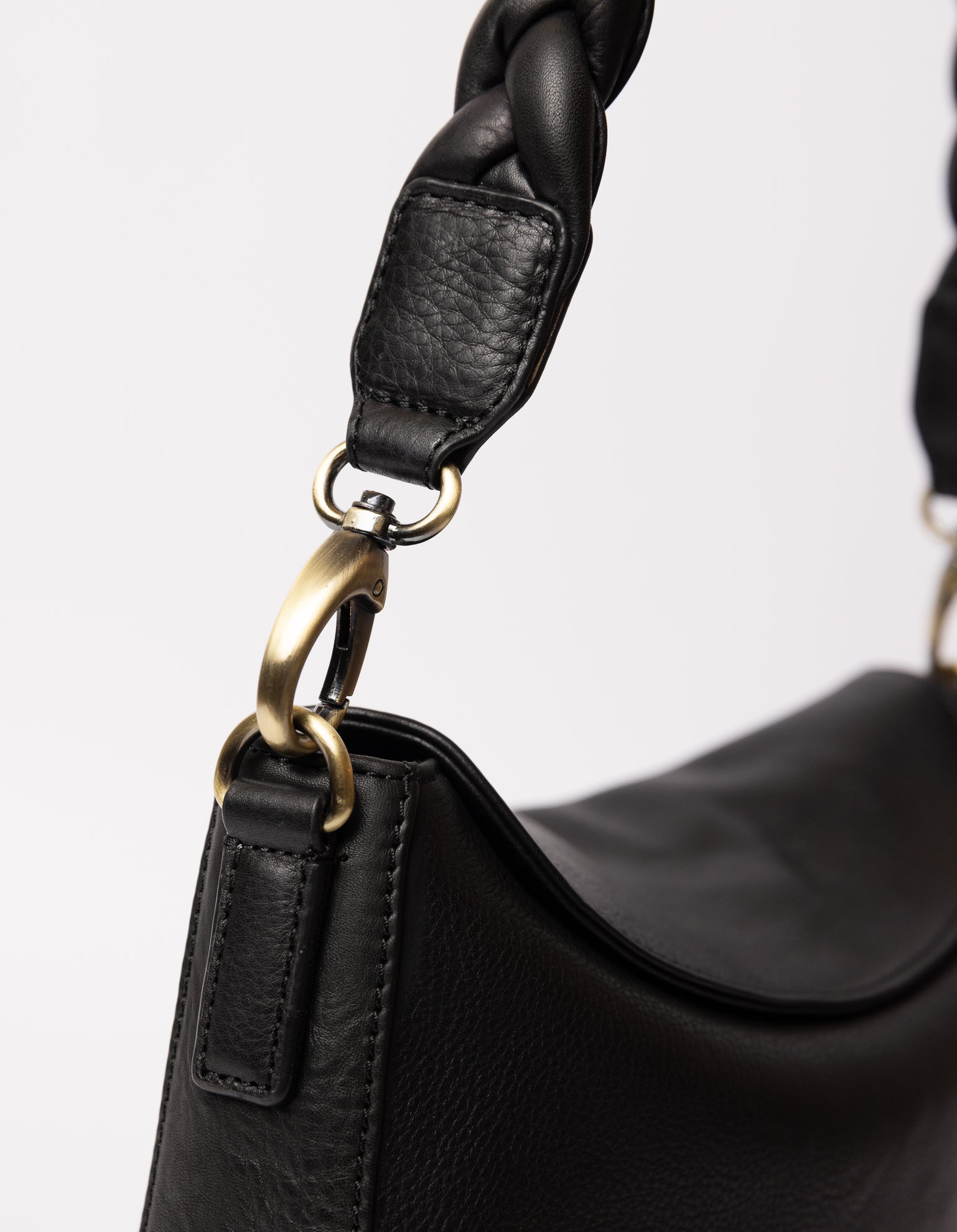 black bag on white background - close up of braided black leather strap hooked on the bag