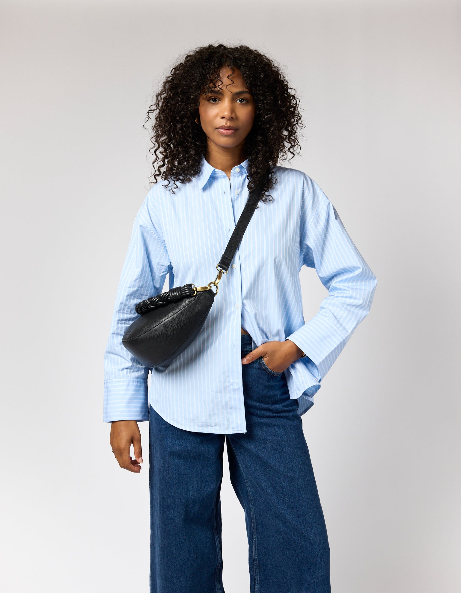 Female model with blue shirt and black leather bag on shoulder with two straps