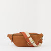 A tan leather fanny pack with a wide, adjustable woven strap in terracotta red and cream, featuring a gold-tone buckle.
