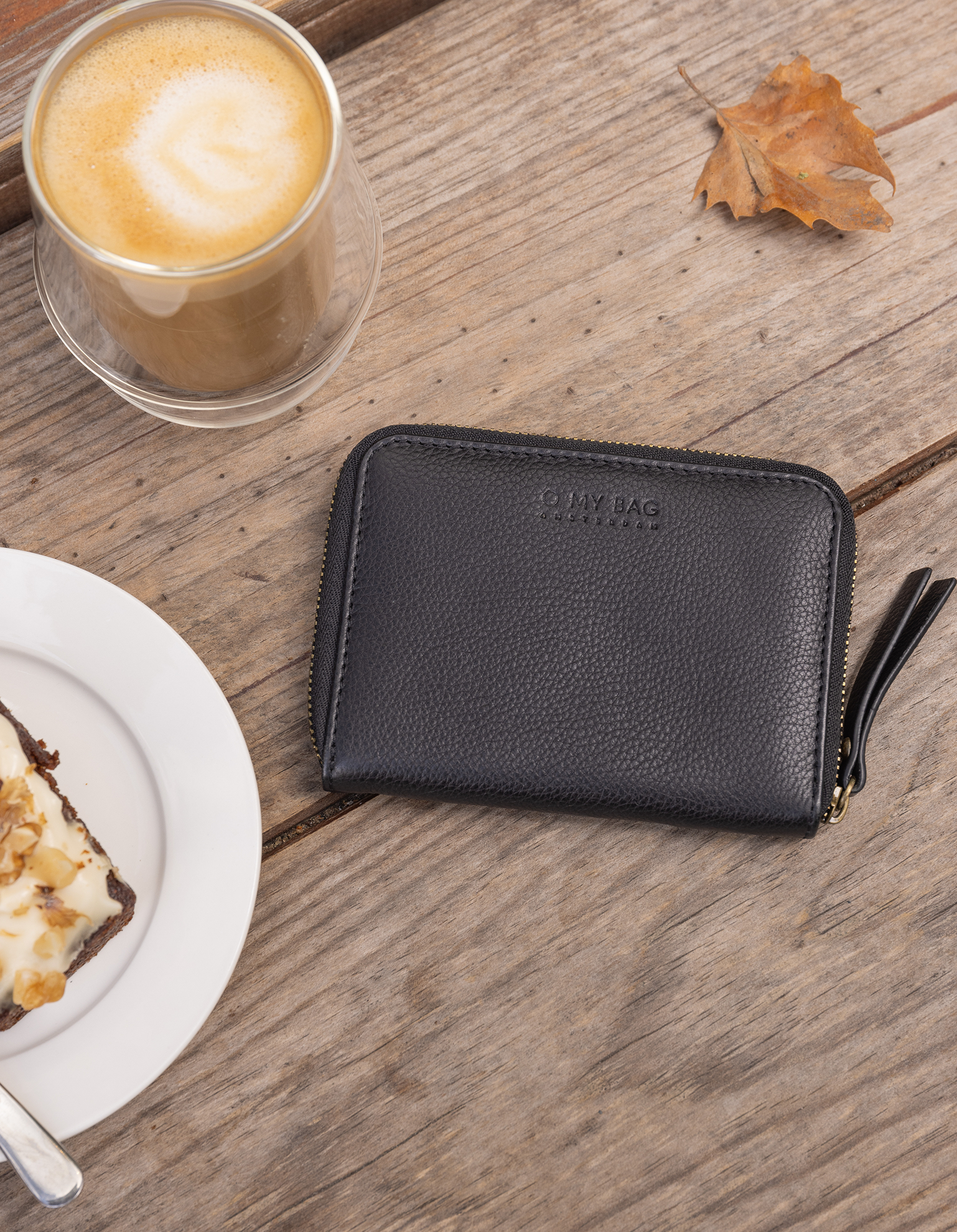 Black leather wallet on wooden table with coffee and cake