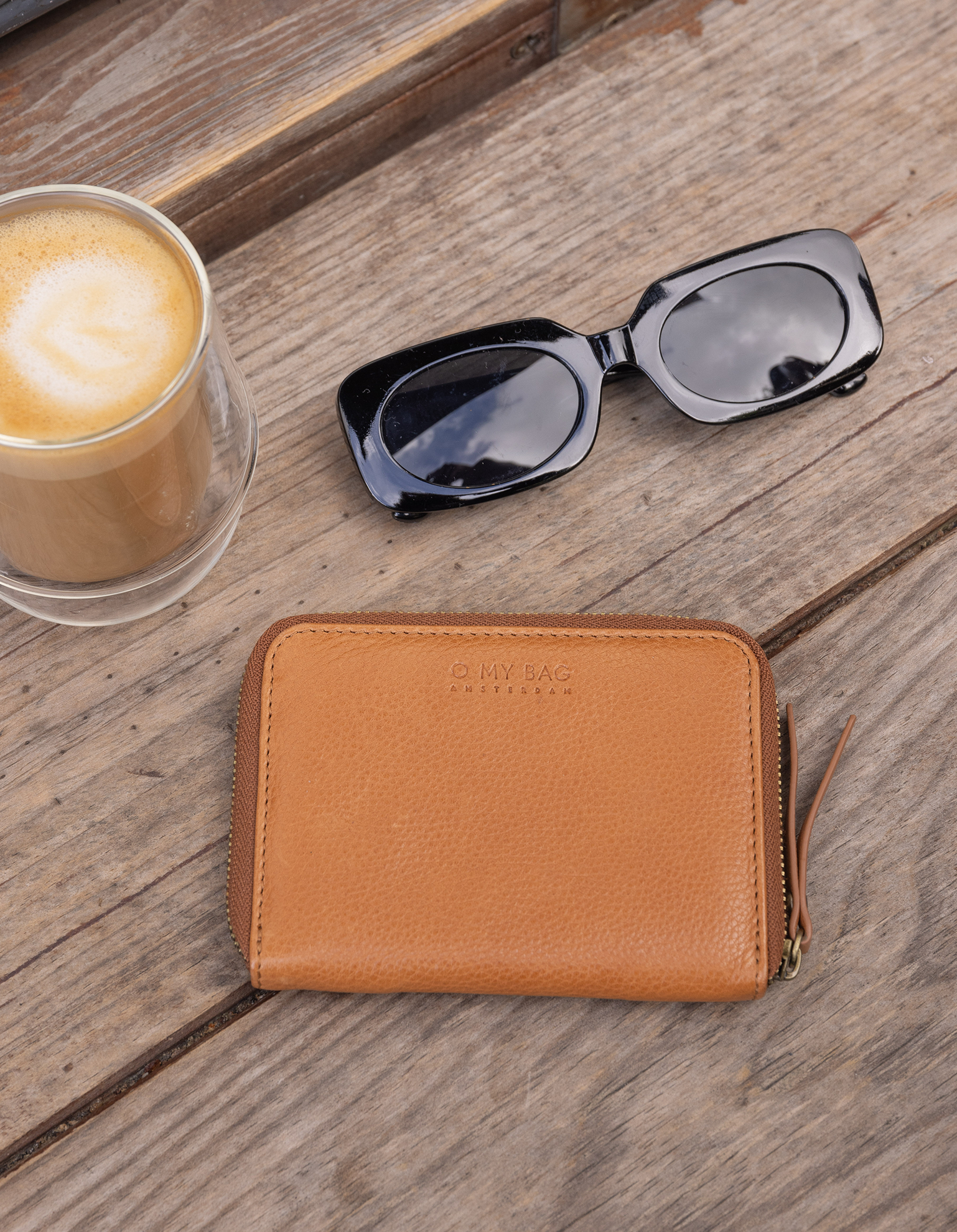 Brown leather wallet on wooden table with coffee and sunglasses