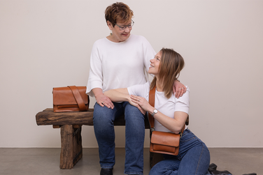 Image of two women sitting together holding brown leather bags