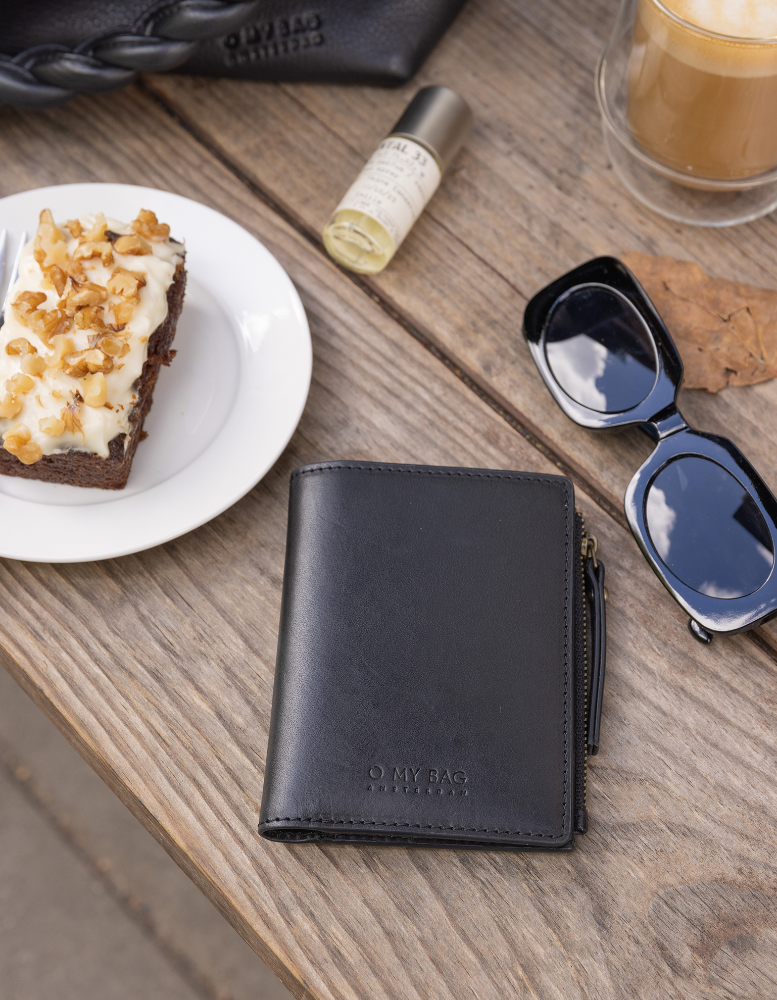 Black leather wallet on wooden table with coffee and cake