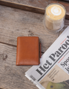 Brown leather wallet on wooden table with coffee and newspaper