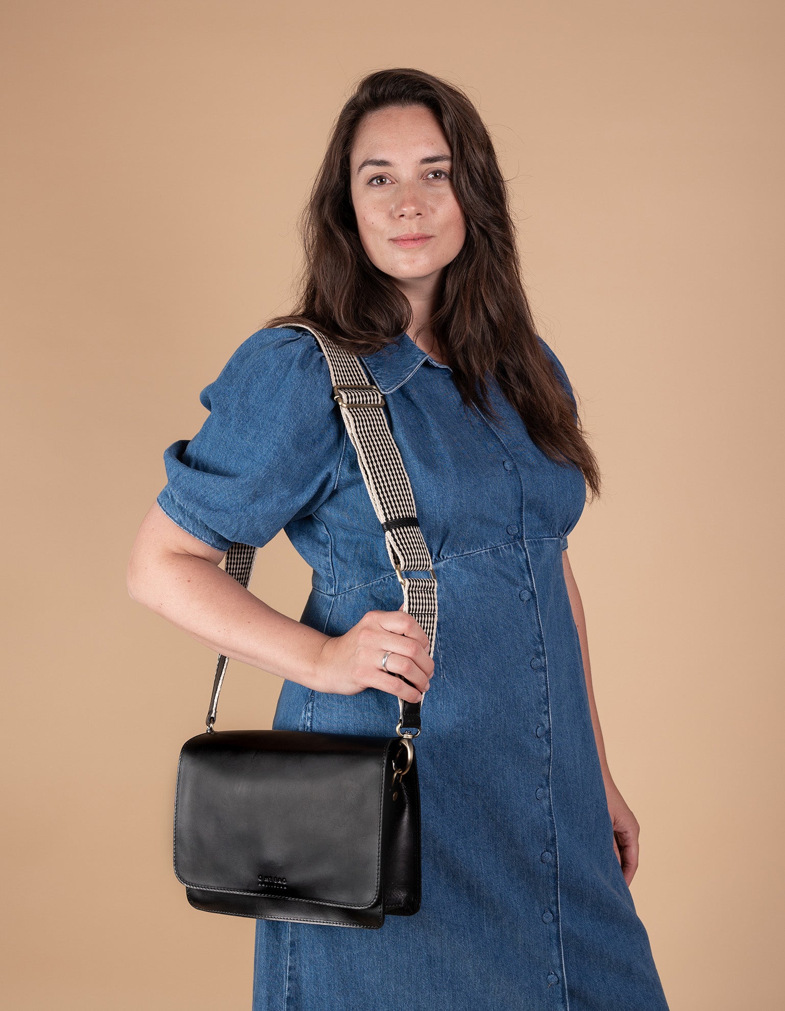Black Leather womens handbag. Square shape with an adjustable webbing strap. Model product image