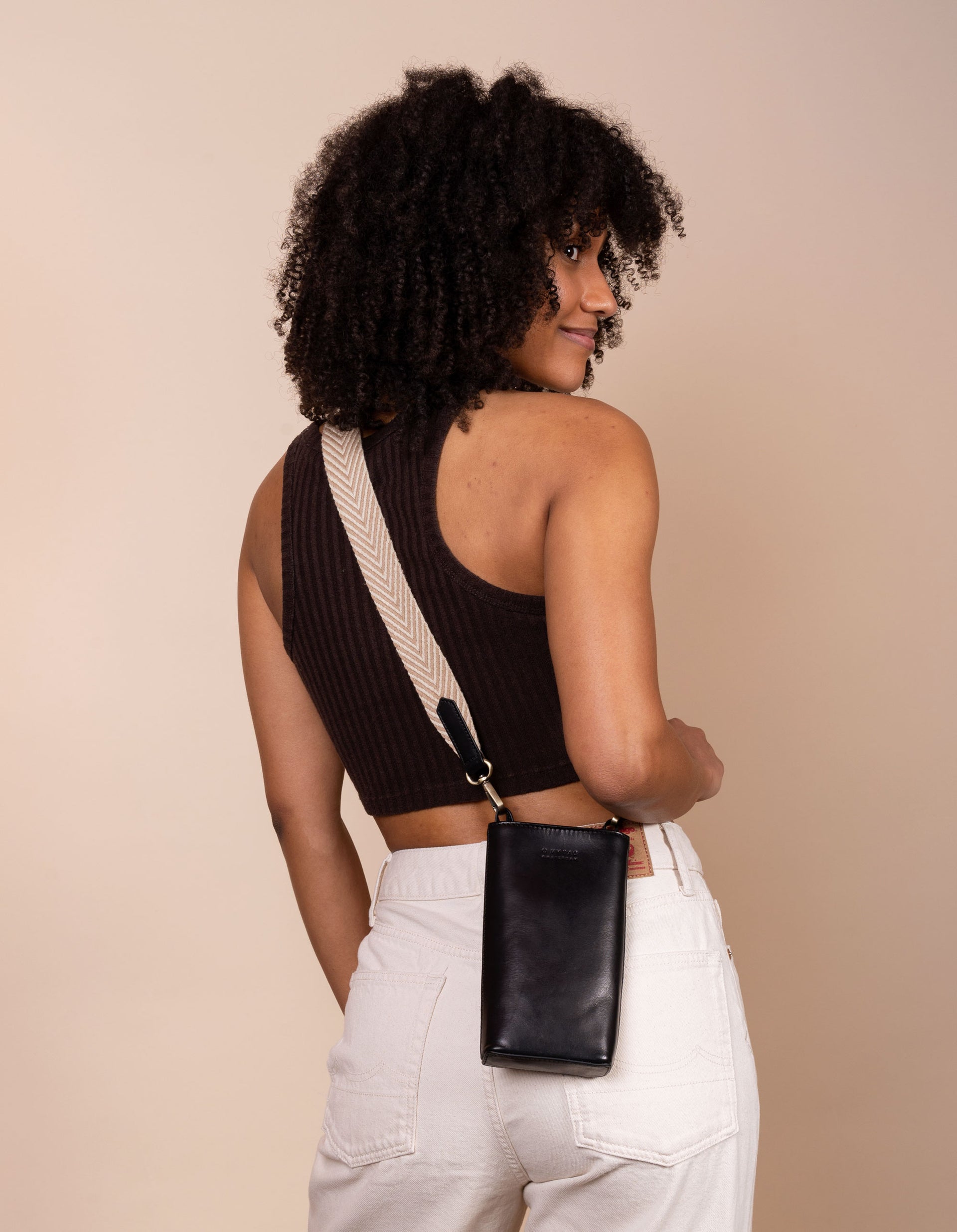 Charlie phone bag - black classic leather - female model product image with the webbing strap - back view