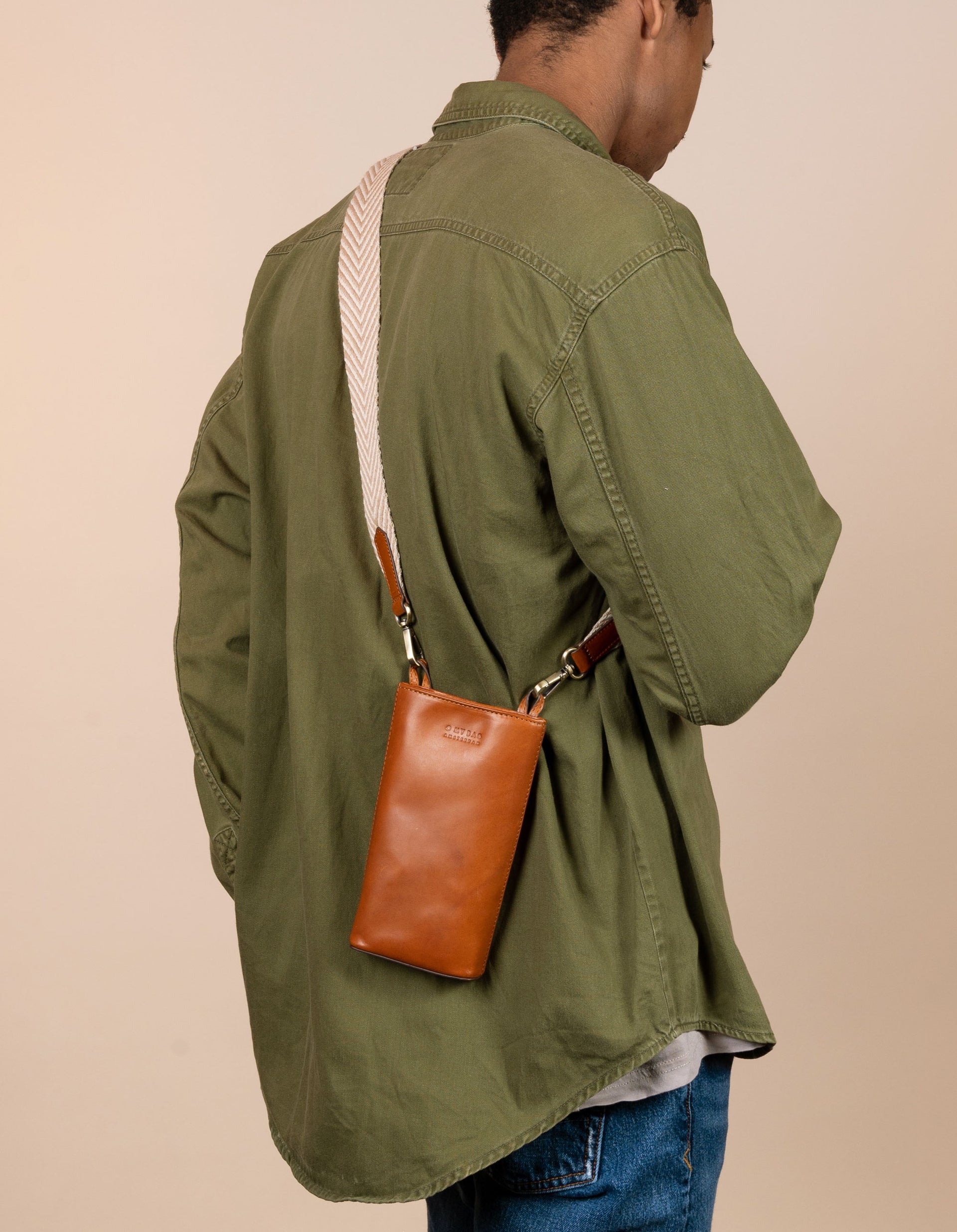 Charlie phone bag - cognac classic leather - male model back product image with organic cotton webbing strap