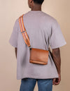 Orange & red adjustable webbing strap with cognac leather details. Male model product image, back view.