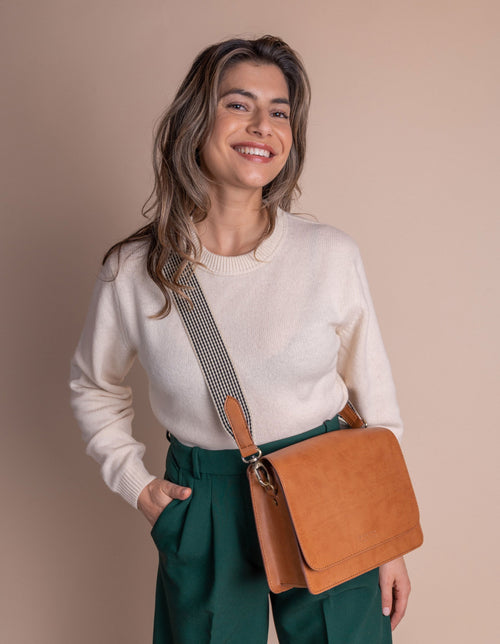 Model with Audrey in cognac apple leather and checked webbing strap.