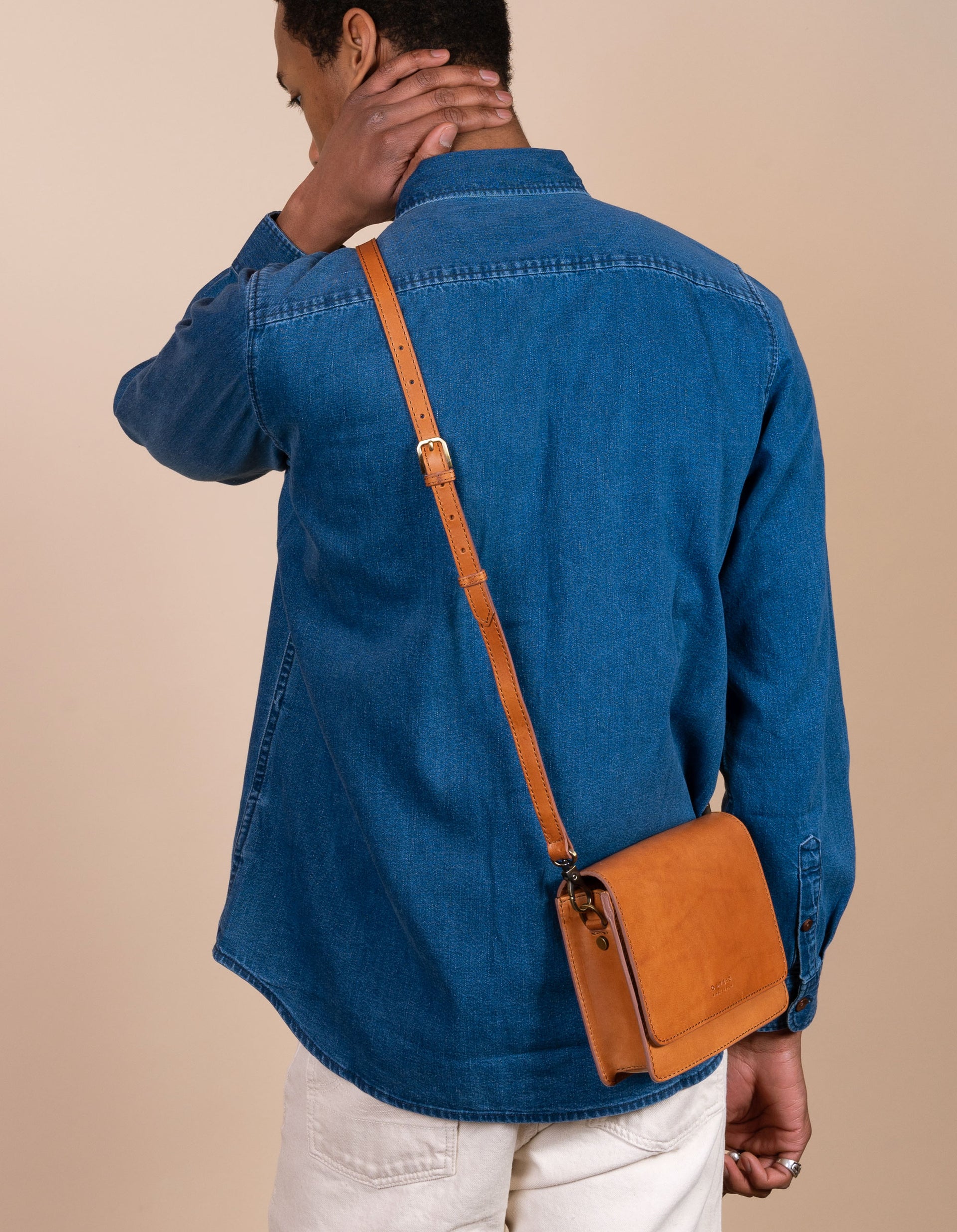 Audrey Mini Cognac leather bag. Square shape with an adjustable leather strap. Male Model image