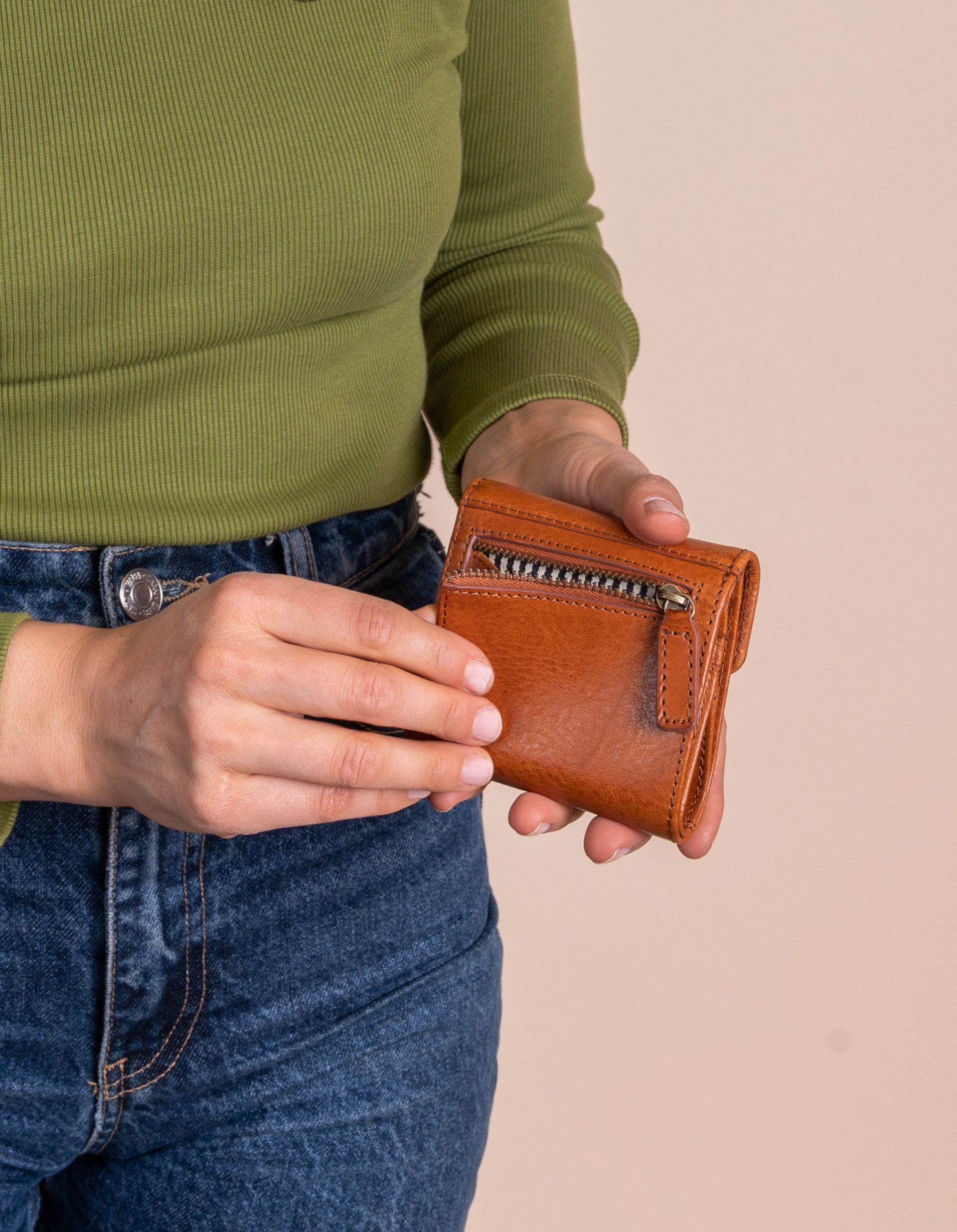 Model holding Georgie's wallet in cognac leather. Showing the back zip pocket.