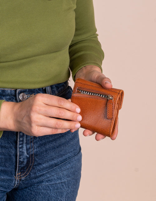 Model holding Georgie's wallet in cognac leather. Showing the back zip pocket.