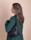 Black Leather womens handbag. Square shape with an adjustable strap. Lifestyle product image.