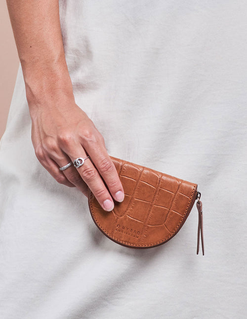 Laura Purse Cognac Classic Croco Leather. Round mood shape coin purse unisex wallet. Model image.