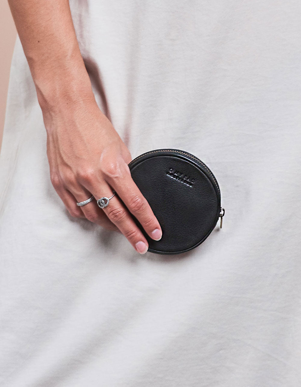 Luna Purse Black Soft Grain Leather. Circular coin purse, wallet for men and women. Model image.