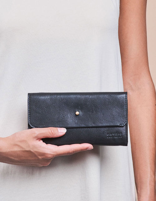 Pixie Pouch Black Soft Grain Leather. Rectangular shaped fold over wallet. Model image.